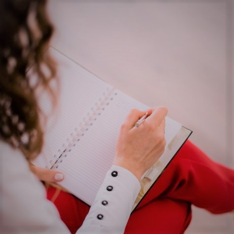Auf dem Foto ist eine weibliche Person zu sehen, die etwas in ein Notizbuch schreibt.