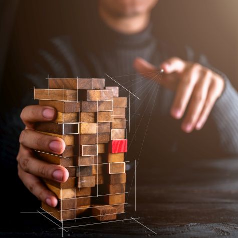 Die Abbildung zeigt einen Geschäftsmann, der einen Holzblock untersucht, bei dem ein einzelner Baustein - als potenzielle Schwachstelle - eine rote Farbe hat
