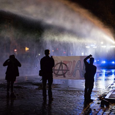 Aktivisten halten bei Nacht in Hamburg ein Transparent, auf dem ein anarchistisches Symbol zu sehen ist.